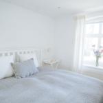 Ein Schlafzimmer mit weißem Bett, Fenster und Blumen auf dem Fensterbrett.