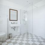 Badezimmer mit Dusche, Waschbecken und Toilette. Fliesenboden mit Schachbrettmuster.