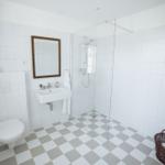 Badezimmer mit Dusche, Waschbecken und Toilette. Fliesenboden und Spiegel.