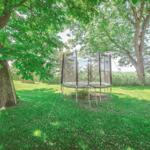 Trampolin mit Sicherheitsnetz im grünen Garten unter Bäumen.