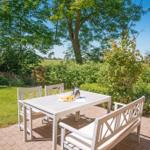 Terrasse mit Tisch und Bänken, umgeben von Grün und Bäumen.