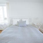 Schlafzimmer mit weißem Bett, zwei Nachttischen und Fenster mit weißen Vorhängen.