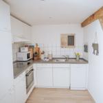 Küche mit weißen Schränken, Spüle und Waschmaschine. Holzbalken an der Wand.