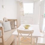 Esszimmer mit weißem Tisch, Stühlen und Sofa. Fenster und Tür führen nach draußen.