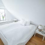 Schlafzimmer mit weißem Bett, Holzboden und Fenster mit Blumen.