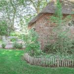 Haus mit Strohdach, Garten mit Tisch und Stühlen, umgeben von Bäumen und Gras.