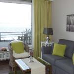 Wohnzimmer mit Sofa, Sessel und Meerblick durch großes Fenster.