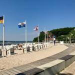 Strand mit Strandkörben, Holzweg und Flaggen am Ufer.