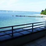 Terrasse mit Blick auf See und Strand. Bootssteg und Segelboote sind sichtbar.