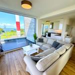 Wohnzimmer mit Sofa, Couchtisch und Blick auf Terrasse und Meer.