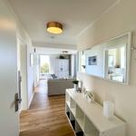 Flur mit Spiegel, Schrank und Blick in Wohnzimmer mit Sofa und Balkon.