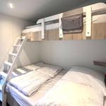 Zimmer mit Doppelbett und obere Schlafcouch, weiße Leiter und Fenster.