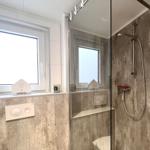 Badezimmer mit Dusche und Fenster. Betonwände und Glasduschtür.