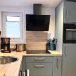 Küche mit Dunstabzug, Herd und Kühlschrank. Holzoberflächen und graue Schränke.