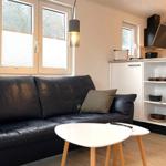 Schwarzes Sofa mit Kissen, weißer Tisch und Küchenbereich mit Schränken.