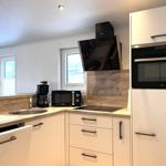 Küche mit Spüle, Herd, Mikrowelle und Backofen. Holzoberflächen und weiße Schränke.