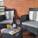 Zwei Sessel mit Kissen und Tisch mit Wein, Gläsern und Buch auf Balkon.