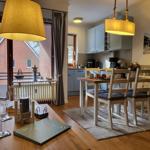 Esszimmer mit Tisch, Stühlen und Küchenbereich. Balkon mit Blick auf Haus.