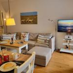 Wohnzimmer mit Sofa, Fernseher und Esstisch mit Speisen.