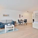 Wohnung mit Sofa, Tisch, Stühlen und Bett. Holzboden und weiße Wände.