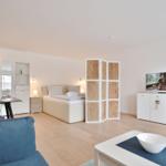 Ein Raum mit Bett, TV und Sitzgelegenheiten auf hellem Holzboden.