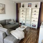 Wohnzimmer mit grauem Sofa, weißen Regalen und Holzboden.