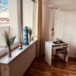 Ein kleiner Schreibtisch mit Stuhl steht neben einem Fenster. Auf dem Fensterbrett stehen Dekorationsgegenstände.