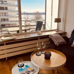 Wohnzimmer mit Blick auf Fluss und Balkon. Holztische, Gläser und Dekoration.