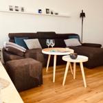 Ein Wohnzimmer mit braunem Sofa, zwei runden Tischen und Holzboden.