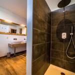 Dusche mit Duschbrause und Handbrause. Toilette und Waschbecken im angrenzenden Raum.