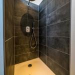 Duschkabine mit dunklen Fliesen und runder Duschkopf