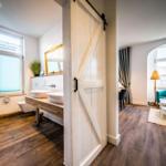 Badezimmer mit Doppelwaschbecken und Schlafzimmer mit grüner Couch.