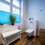 Badezimmer mit Toilette, Fenster, Bänkchen und Korb.