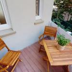 Terrasse mit Holztisch, zwei Stühlen und Pflanze. Hintergrund mit Grün und Zaun.