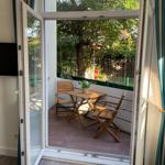 Terrasse mit Tisch und zwei Stühlen, umgeben von Bäumen und einem Zaun.