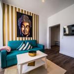 Wohnzimmer mit türkisfarbenem Sofa, Wandbild Buddha und Fernseher an der Wand.