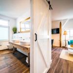 Badezimmer mit Doppelwaschbecken und Wohnzimmer mit türkisfarbenen Sofas.