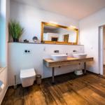 Badezimmer mit Doppelwaschbecken, Spiegel und Holzboden.