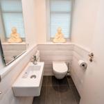 Badezimmer mit Waschbecken, Toilette und Buddha-Statue auf Fensterbank.
