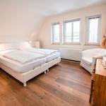 Schlafzimmer mit Doppelbett, Holzboden und Fenstern.