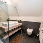 Badezimmer mit Dusche, Waschbecken und Toilette. Schwarze Fliesen und Holzoberflächen.