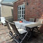 Terrasse mit Holztisch, Stühlen und Sonnenschutz. Tisch gedeckt mit Wein und Obst.