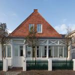Haus mit rotem Ziegeldach und weißem Vordach. Grün gestrichener Zaun vor der Eingangstür.