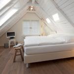 Schlafzimmer mit Dachschrägen, Bett, Fenster und Holzboden.