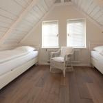 Zimmer mit zwei Betten, Holzboden und Dachschräge mit Fenstern.