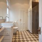 Badezimmer mit Dusche, Waschbecken und Toilette auf schwarz-weißem Fliesenboden.