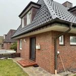 Rotes Backsteinhaus mit Dachgauben und Vorgarten. Eingang mit Briefkasten und Gartenwerkzeug.