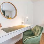 Schreibtisch mit grünem Sessel und runden Spiegel an der Wand.
