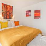 Schlafzimmer mit Bett, Kissen und Wandbildern.