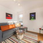 Ein Wohnzimmer mit grauem Sofa, bunten Kissen und Wandbildern.